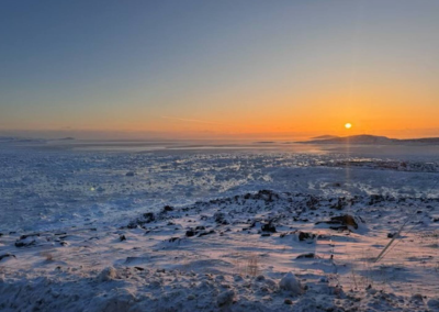 Golden Arctic winter sunset over the frozen expanse of Frobisher Bay in Iqaluit, Nunavut, with snow-covered tundra and ice stretching to the horizon.