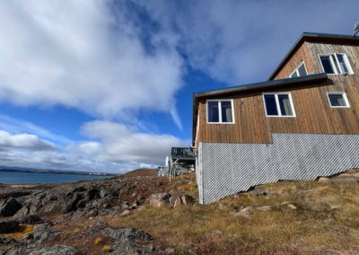 Backside of Stay by the Sea B&B in Iqaluit, Nunavut, perched on the rocky Arctic tundra with views of Frobisher Bay under a wide, partly cloudy sky.