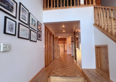 Main entrance hallway and wooden stairwell at Stay by the Sea B&B in Iqaluit, Nunavut, featuring high ceilings, framed artwork, wood accents, and access to guest rooms on the second floor.