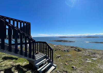 Stairs leading from the back deck of Stay by the Sea B&B in Iqaluit down to the Arctic tundra, with sweeping views of Frobisher Bay under a bright blue summer sky