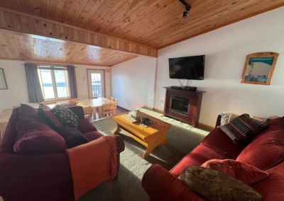 Cozy common area at Stay by the Sea B&B in Iqaluit with lots of natural light to bask in while enjoying plush red sofas, a fireplace, and natural wood finishes