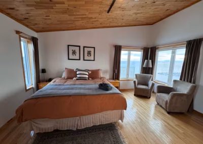 Room 2 located on the second floor at Stay by the Sea B&B in Iqaluit featuring a spacious king bed, wooden dresser, and large corner windows providing a stunning view of Frobisher Bay