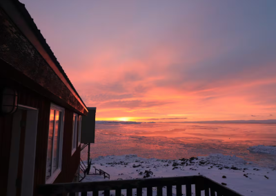 Vibrant Arctic sunset over Frobisher Bay, viewed from the back deck of Stay by the Sea B&B in Iqaluit, Nunavut, with pink and orange skies reflecting off snow and ice.